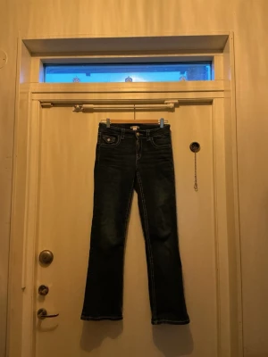 Bootcut jeans från Gina Tricot - Mörkblå bootcut jeans från Gina Tricot med kontrastsömmar och klassisk femficksdesign. Baksidan har fickor med lock och knappdetalj. Jeansen har dragkedja och knapp framtill, samt bälteshällor. De är uppsydda och passar någon som är 155-163cm. Om fler bilder önskas är det bara att skriva..