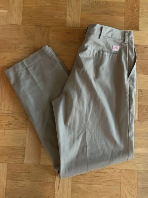 Beige chinos från Red Kap - Snygga beige chinos från Red Kap med lös passform och diskret logga ovanför bakfickan. Byxorna har bälteshällor och är gjorda i mjuk bomull som känns skön mot huden. Perfekta för dig som gillar stilrena och enkla byxor.