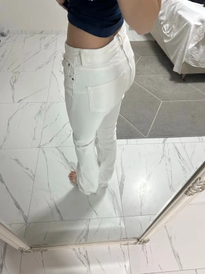 Vita utsvängda  jeans från Zara, strl 40 - Säljer ett par vita jeans från Zara i storlek 40. De har utsvängda ben, klassisk femficksmodell och en mid waist. Materialet är bomull med en mjuk känsla och de har snygga silverfärgade nitar vid fickorna. Perfekta till en clean och fräsch look.