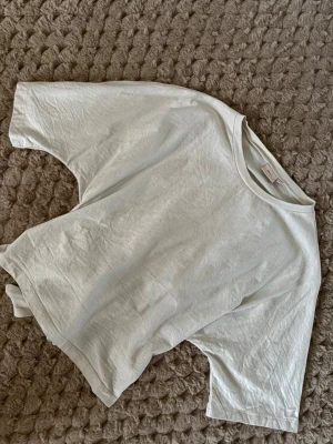 Vit omlottopp med knyt från Nelly - Säljer en vit omlottopp från Nelly i storlek L. Toppen har korta ärmar, rund halsringning och snygg knytning i ryggen som ger en cool detalj. Materialet är mjuk bomull och modellen är loose fit för en avslappnad vibe.