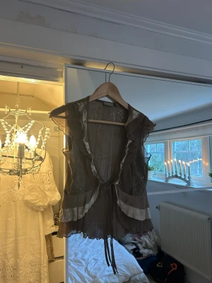 Brun omlottväst med spets och volang - Supersöt brun väst med omlottknytning framtill, volangdetaljer och spets. 