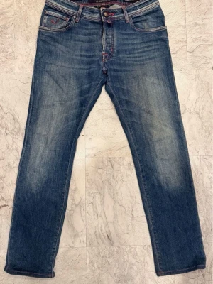 Jacob Cohën jeans! 🇮🇹 size 30 (622/Nick) - Snygga blå jeans från Jacob Cohën, modell Style 622. Jeansen har röd kontrastsöm, klassisk femficksdesign och knappgylf. Materialet är slitstark bomull med en tvättad look. Passformen är rak och normal, perfekt för dig som gillar stilrena detaljer.