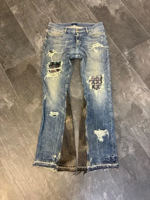 MARES TAKEOVER 1 OF 1 ”GARDEN” - Säljer ett par blå bootcut jeans från Levi's med slitna detaljer och stora hål som är patchade med färgglada, mönstrade tygbitar. Jeansen har fransiga benslut och en cool vintage vibe. Perfekt för dig som gillar unik streetstyle och vill sticka ut.