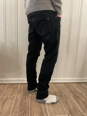 Svarta dondup jeans - Säljer ett par svarta jeans från Dondup med klassisk passform (modell George). Jeansen har en snygg mörk tvätt, raka ben och detaljerad bakficka med Dondup-logga. Perfekta för dig som gillar stilrena och bekväma jeans. (Stora i midjan på modellen därför ser de lite konstiga ut i rumpan)