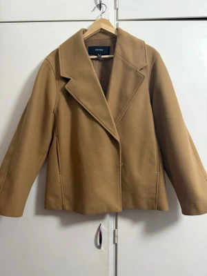 Beige kappa från Vero Moda, M - Snygg beige kappa från Vero Moda i storlek M. Jackan har klassisk krage, raka långa ärmar och en enkel knappstängning framtill. Materialet är mjukt och har en ull-liknande känsla, perfekt för höst och vinter. Stilren och enkel design som är lätt att matcha.