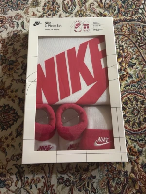 Vit och röd Nike babyväst - Nike babyväst,skor och även mössa i vitt med stor röd logga framtill. Västen har en klassisk, sportig look och är tillverkad i mjuk bomull och polyester(skorna och mössan också). Perfekt för små trendsetters som gillar streetstyle. Säljes i originalförpackning.