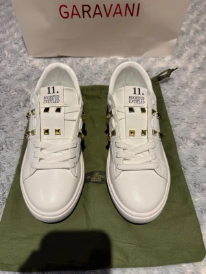 Valentino Rockstud Untitled vita sneakers - Säljer ett par vita Valentino Rockstud Untitled sneakers med coola guldfärgade nitar på sidorna. Märket syns tydligt på plösen och sulan. Perfekt för dig som gillar lyxiga detaljer och streetstyle. Skulle också kunna vara perfekta presenten till en nära.🙌🙌