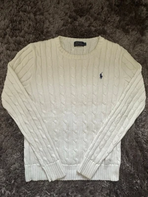 Äkta Vit kabelstickad tröja Polo Ralph Lauren - Säljer en vit kabelstickad tröja från Polo Ralph Lauren i storlek S. Tröjan har rund hals, långärmade ribbade muddar och den klassiska broderade loggan på bröstet. Perfekt för dig som gillar stilrena och tidlösa plagg med snygg struktur. Äkta‼️