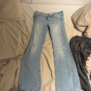 Ljusblå bootcut jeans från Gina Tricot - Säljer ett par ljusblå bootcut jeans från Gina Tricot i storlek 164. Jeansen har slitna detaljer på benen och klassisk femficksdesign. De är tillverkade i mjukt denimtyg och har en snygg, lite utsvängd passform nertill.