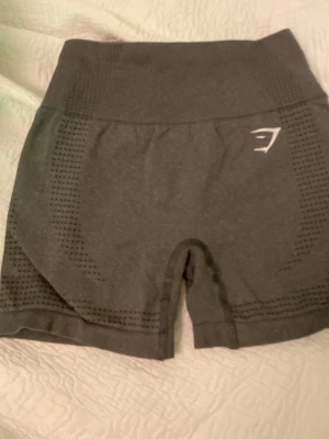 Mörkgrå seamless shorts från Gymshark - Säljer ett par mörkgrå seamless shorts från Gymshark med hög midja och diskret hålmönster längs sidorna. Stretchigt material som sitter tight och följer kroppen perfekt. Perfekta för träning eller gymmet.