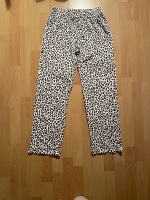 Leopardmönstrade pyjamasbyxor - Leopardmönstrade pyjamasbyxor som är vita med svarta och gråa leopardfläckar och har elastisk midja.