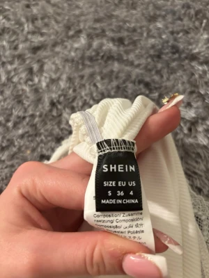 Vit bandeau tubtopp med spets från SHEIN - Säljer en vit bandeau tubtopp från SHEIN i storlek S. Toppen är ribbad och har en söt spetskant upptill med en liten rosett i mitten. Materialet är mjukt och stretchigt , perfekt för sommarens alla tillfällen. Dock är materialet lite tunt.💕