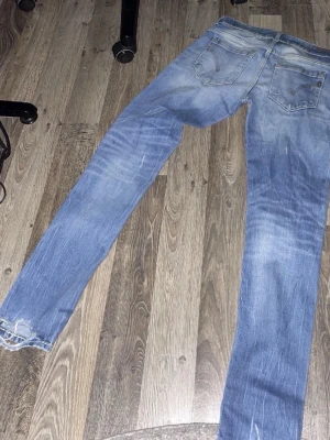 Blå dondup jeans - Säljer ett par blå jeans från Levi's med slitningar och hål på framsidan för en cool och avslappnad look. Jeansen har klassiska fem fickor, knappgylf och raka ben. Materialet är robust denim i bomull och passformen är normal.