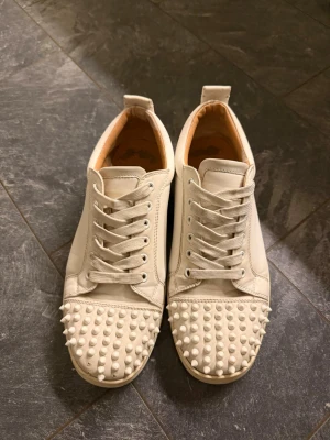 Christian Louboutin Louis Junior Spikes - Säljer ett par vita sneakers med nitar på tån. Storlek 42 men sitter som storlek 44 Skorna har andvänts så slitage finns, 5 nitar är borta på högra skon, den vänstra har alla nitar kvar. Säljes som dem är, det vill säga ingen låda eller certifikat därav priset. Priset är inte hugget i sten.