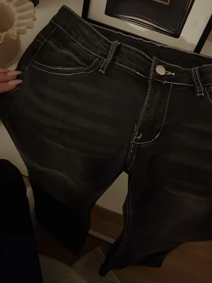 Svarta bootcut jeans med kontrastsömmar - Snygga svarta jeans med tydliga vita kontrastsömmar och klassisk femficksdesign. Modellen har bootcut-ben och en knappstängning fram. Materialet är jeans och de har en jätte bra passform💕