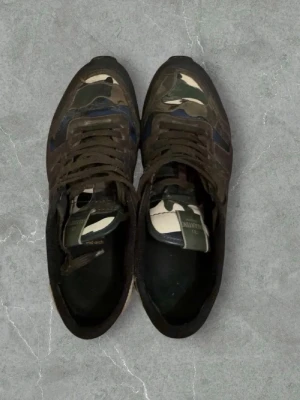 Valentino Rockrunner sneakers camouflage - Säljer ett par Valentino Rockrunner sneakers med klassiskt camouflage-mönster i grönt, beige och brunt. Skorna har snörning, platt sula och rund tå. Materialmix med inslag av mocka och skinn. Perfekta för dig som gillar streetstyle och exklusiva märken.