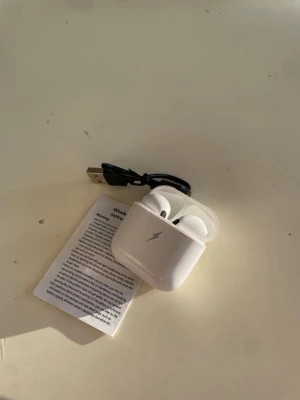 Trådlösa hörlurar med laddningsetui - Snygga trådlösa hörlurar med laddningsetui, USB-laddkabel och instruktionsmanual. Hörlurarna är vita och har en modern design. Passar perfekt för musik och samtal. Produkten ser ut att vara i gott skick utan synligt slitage eller defekter.