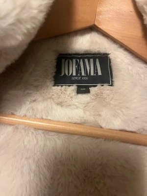 Svart parkajacka med teddyfoder från Jofama - Parkajacka från Jofama i svart med mjukt, ljust teddyfoder och huva. Jackan har långa ärmar, dragkedja och tryckknappar framtill samt praktiska fickor. Perfekt för kalla dagar när du vill vara både varm och snygg. Den är aldrig använd bara testad en gång.