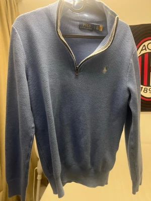  Polo Ralph Lauren - Snygg blå stickad tröja från Polo Ralph Lauren med halv dragkedja och ribbad krage med vit rand. Klassisk logga broderad på bröstet. Långärmad och perfekt för lager-på-lager under höst och vinter. Passar dig som gillar stilrena och tidlösa plagg.