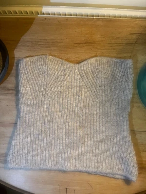 Stickad beige bandeau tubtopp - Säljer en stickad bandeau tubtopp i ljusbeige färg med ribbad struktur. Toppen är axelbandslös. Perfekt att styla med jeans eller kjol för en trendig outfit.