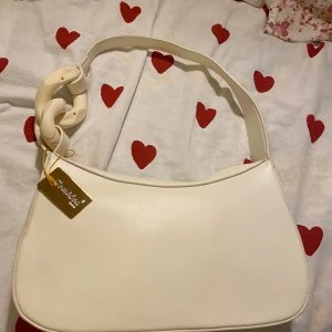 Beige axelväska från Tom&Eva Paris - Säljer en stilren beige axelväska från Tom&Eva Paris med mjuk, slät yta i syntetmaterial. Väskan har en bred axelrem med chunky kedjedetalj i matchande beige ton. Perfekt för dig som gillar minimalistisk design och snygga accessoarer. Helt ny, aldrig använt med prislapp kvar. Köptes för 549kr 