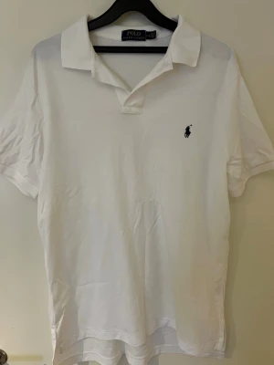 Vit pikétröja från Polo Ralph Lauren - Säljer en klassisk vit pikétröja från Polo Ralph Lauren med korta ärmar och krage. Tröjan har den ikoniska broderade loggan på bröstet och är gjord i mjuk bomull. Perfekt för dig som gillar stilrena och tidlösa plagg.