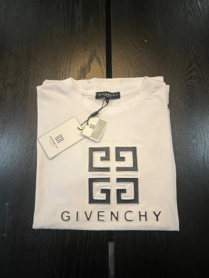 Vit Givenchy t-shirt med tryck - Snygg vit t-shirt från Givenchy med klassiskt svart logotryck på bröstet. Rund hals och korta ärmar. Materialet känns mjukt och skönt, perfekt för en clean och stilren look. Taggarna sitter kvar för extra lyxig känsla.