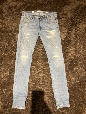 Replay Bronny ljusblå super slim jeans - Säljer ett par Replay Bronny jeans i slim fit med ljusblå tvätt och slitna detaljer. Jeansen har klassisk femficksdesign, broderad Replay-logga vid fickan och röd R-detalj.