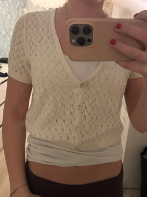 Vit kortärmad kofta med knappar - Söt vit kofta med korta ärmar och v-ringning. Koftan har ett genomgående hålmönster och stängs med små knappar framtill. Perfekt att slänga över ett linne för en fräsch look.