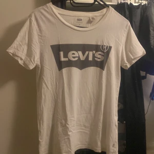 Vit t-shirt från Levi's - Säljer en klassisk vit t-shirt från Levi's med deras ikoniska logga i svart på framsidan. T-shirten har en rund hals och korta ärmar, perfekt för en avslappnad stil.