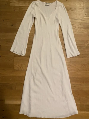 Vit ribbad långklänning från AWARE - Säljer en stilren vit långklänning från AWARE med ribbad struktur och sweetheart urringning. Klänningen har långa ärmar och är figurnära upptill med lätt utsvängd nederdel. Perfekt för dig som gillar enkel och snygg design.