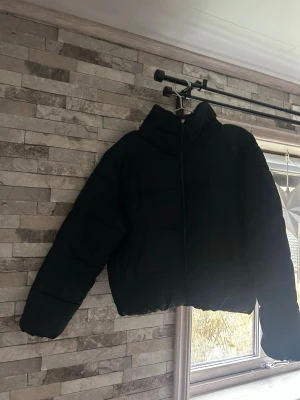 Svart pufferjacka med dragkedja - Säljer en svart pufferjacka med hög krage och hel dragkedja framtill. Jackan har en loose passform och är quiltad för extra värme. Perfekt för kalla dagar och enkel att matcha med olika outfits.