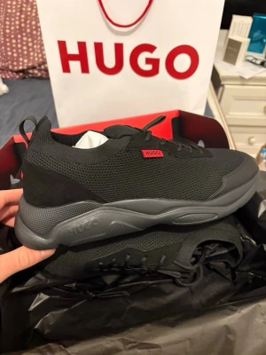 Svarta sneakers från Hugo Boss strl 44 - Säljer ett par svarta Hugo Boss sneakers i storlek 44. Aldrig använda, köpta för 2100kr. Perfekta för dig som gillar stilrena och moderna sneakers.