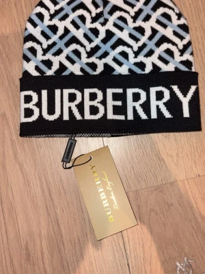 Burberry mönstrad mössa i svart och vit - Snygg mössa från Burberry med grafiskt mönster i svart, vit och ljusblå. Stor logotyp framtill och klassisk Burberry-tag på insidan. Stickad i mjukt material som håller dig varm och stilren under kalla dagar.