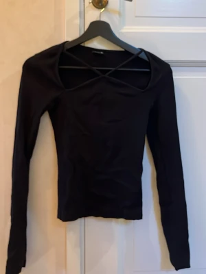 Svart långärmad topp från Gina Tricot - Säljer en svart långärmad topp från Gina Tricot i storlek XS. Toppen har snygga korsade band över bröstet och är figurnära i modellen. Materialet är ribbad och ger en cool struktur. Perfekt att styla med jeans eller kjol för en trendig look.