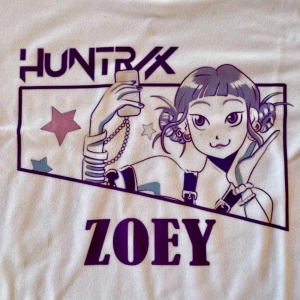 Vit croppad KPop Demon Hunters t-shirt ZOEY - Cool vit croppad t-shirt med lila anime-tryck och texten 'HUNTRX ZOEY' framtill. Kortärmad modell med rund hals och figurnära passform. Perfekt för KPop Demon Hunters fans! 