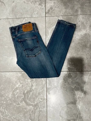 Replay Anbass jeans - Replay Anbass jeans i klassisk blå denim med snygga slitningar och dragkedja. Modellen heter anbass, perfekt för dig som gillar stilrena och bekväma jeans. Storleken är i L32 och W32.