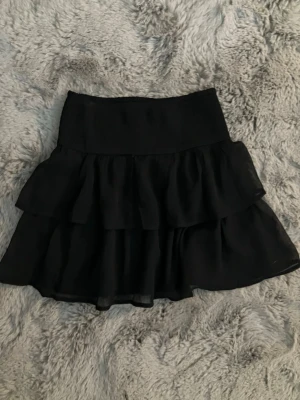 Jättefin Svart volangkjol! - Säljer en svart kortkjol med dubbla volanger! Det är ett jätteskönt material och den svalkar på sommarn samtidigt som den är jättefin! Passar ju även till fester och varma sommardagar! 