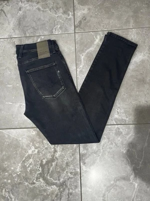 Replay Anbass jeans - Replay Anbass jeans i svart tvätt. Jeansen har dragkedjegylf, smal passform och är tillverkade i stretchig bomullsblandning för extra komfort. Perfekta för en stilren och modern look. Storleken är i L32 och W33.