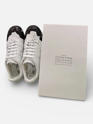 Maison Margiela vita sneakers med svart splash - Maison Margiela sneakers i vitt skinn med svart splash-effekt på tån och svarta prickar över hela skon. Klassisk låg modell med rund tå och snörning. Snygg och unik design som sticker ut, levereras med originalkartong.