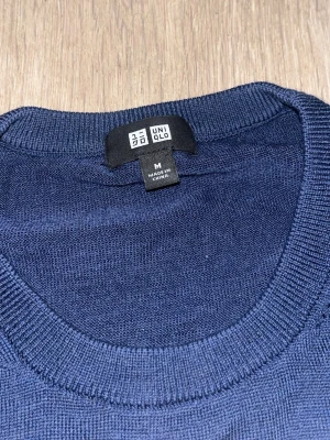 Mörkblå stickad tröja från Uniqlo - Snygg mörkblå stickad tröja från Uniqlo i storlek M. Tröjan har rund hals och långa ärmar med ribbade muddar vid hals, ärmslut och nederkant. Perfekt för dig som gillar stilrena och enkla plagg med skön passform.