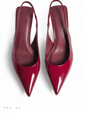 Vinröda pumps med spetsig tå från NAKD - Säljer ett par eleganta vinröda pumps från NAKD med spetsig tå och slingback-rem. Skorna har en låg klack och är tillverkade i glansigt syntetmaterial som ger en lyxig känsla. Perfekt för dig som gillar stilrena och trendiga skor med lite extra edge.