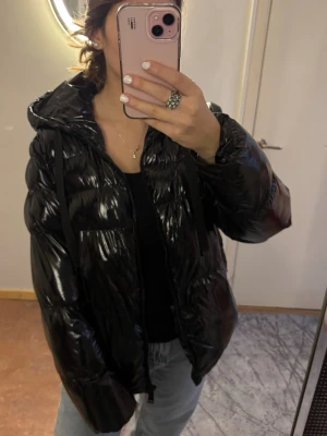 Svart glansig jacka  från Guess - Säljer en glansig svart pufferjacka från Guess med huva och dragkedja. Perfekt nu till vintern💓💓💓 Nypris: 2500kr
