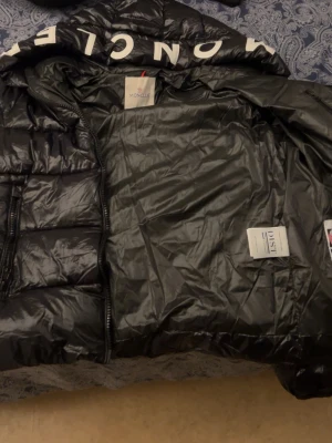 Svart Moncler pufferjacka med huva - Säljer en svart pufferjacka från Moncler eftersom att den är för liten på mig och för kort