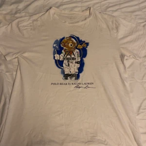 Vit t-shirt med Polo Bear astronaut från Ralph Lauren - Vit t-shirt från Ralph Lauren med Polo Bear i astronautdräkt tryckt på bröstet.