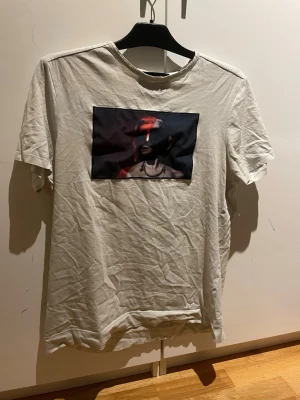 Vit t-shirt med tryck från Limitato - Vit t-shirt från Limitato med ett stort konstnärligt tryck på bröstet i svart och rött. Klassisk rund hals och korta ärmar. Mjuk bomullskänsla och diskret Limitato-logga i nacken. Perfekt för dig som gillar unika prints.