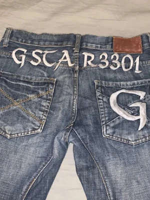 G-Star baggy jeans  - Säljer ett par G-Star 3301 jeans med stora vita broderade bokstäver och siffror på bakfickorna. Jeansen har en baggy passform. Säljer då jag inte använder dem särskilt mycket längre, bra skick med lite slit längst nere. 2000s modell, storlek M/L