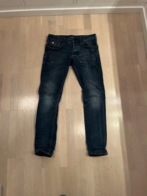 Mörkblå jeans från Scotch & Soda - Säljer ett par mörkblå jeans från Scotch & Soda med snygga slitningar och detaljer vid fickorna. Jeansen har en cool faded effekt på benen. W28 L32