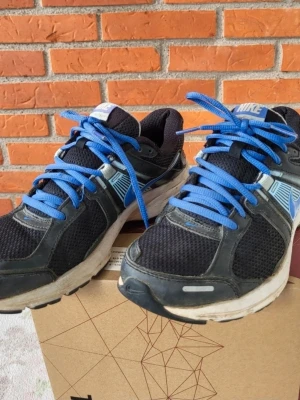 Nike svarta sneakers med blå detaljer 38 - Säljer ett par svarta Nike sneakers med blå swoosh och blå snören. Skorna har mesh- och syntetpaneler för bra andningsförmåga och komfort. Mellansulan är vit och yttersulan är slitstark. Perfekta för träning eller vardagsstil.