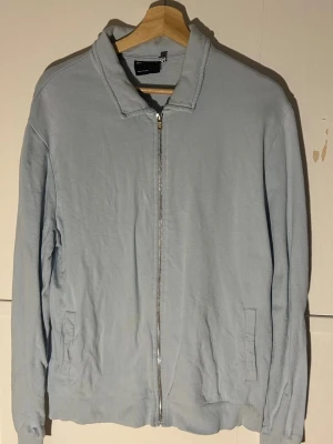Ljusblå ziptröja från ASOS DESIGN - Ljusblå tröja från ASOS DESIGN i mjuk bomullsblandning. Jackan har hel dragkedja framtill, ståkrage och två fickor på sidorna. Perfekt för lager-på-lager och enkel att matcha med olika outfits.